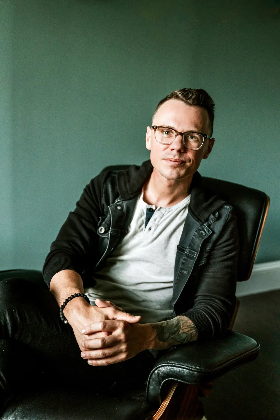 Robbie Poe seated in a black leather chair against a green wall
